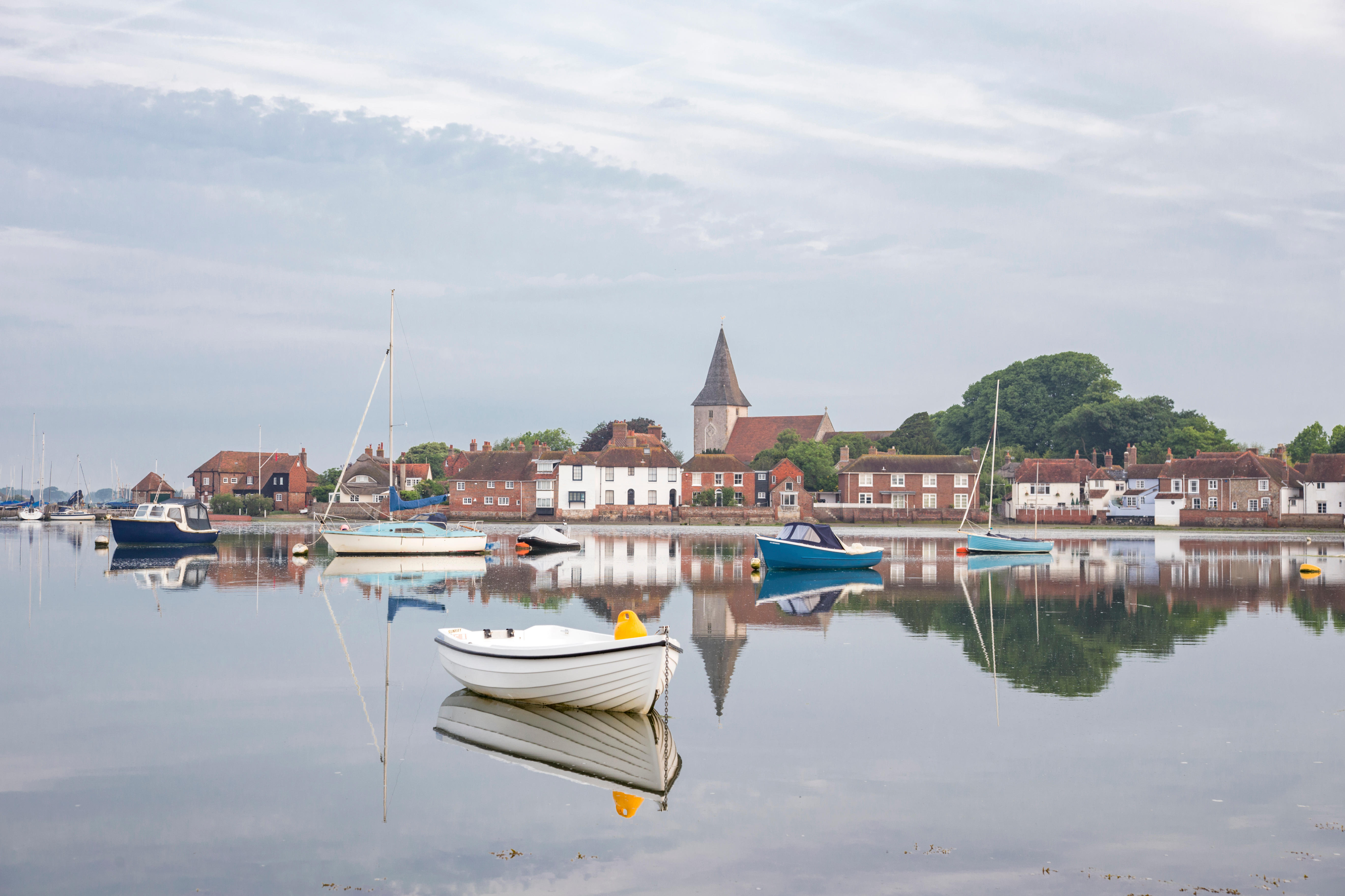 Bosham village, West Sussex, England, reflected in calm harbor waters with several boats.