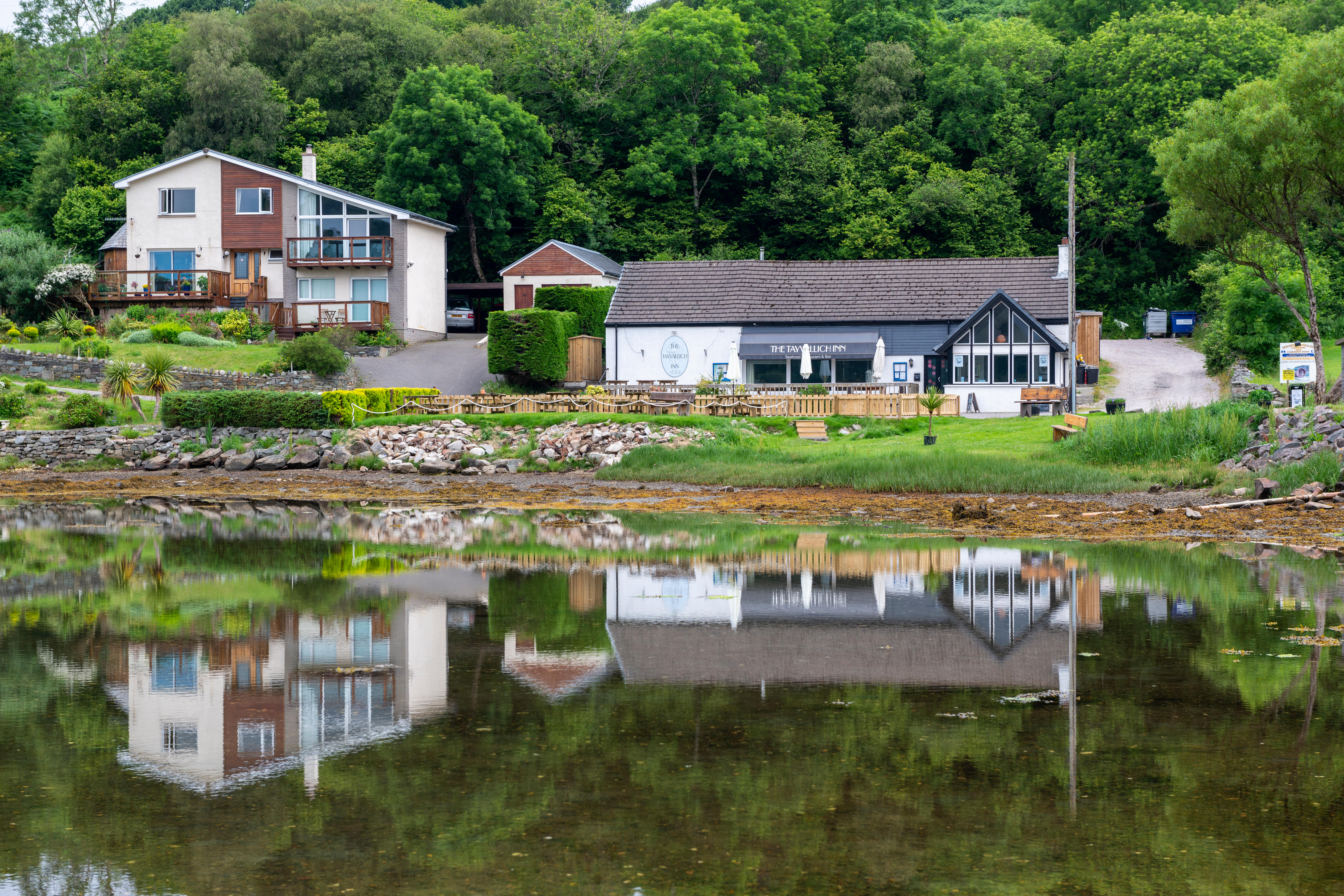 Reflection of Tayvallich Inn and houses in Loch Sween, Scotland.