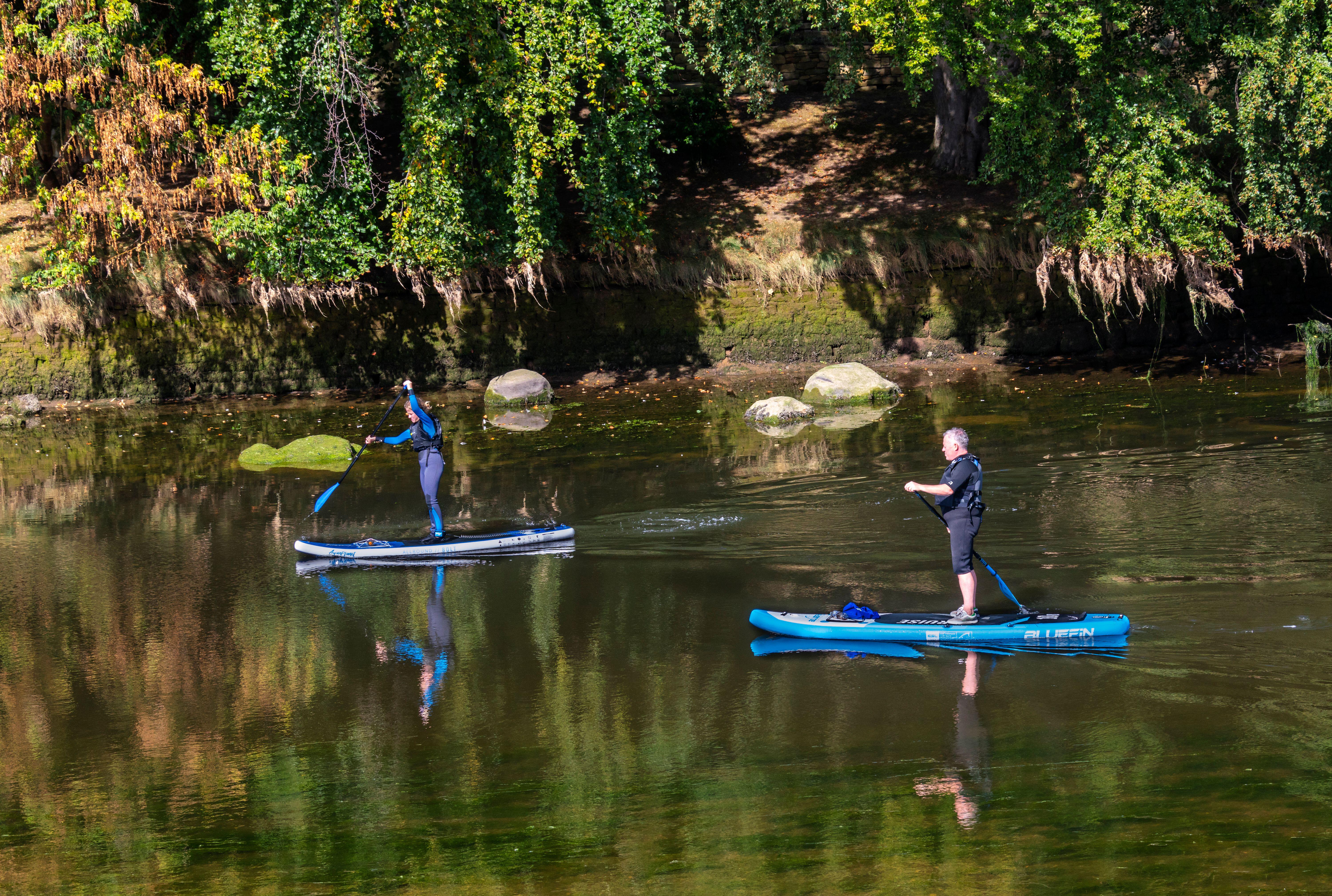 Two people paddleboarding on the River Coquet in Warkworth, Northumberland, England.