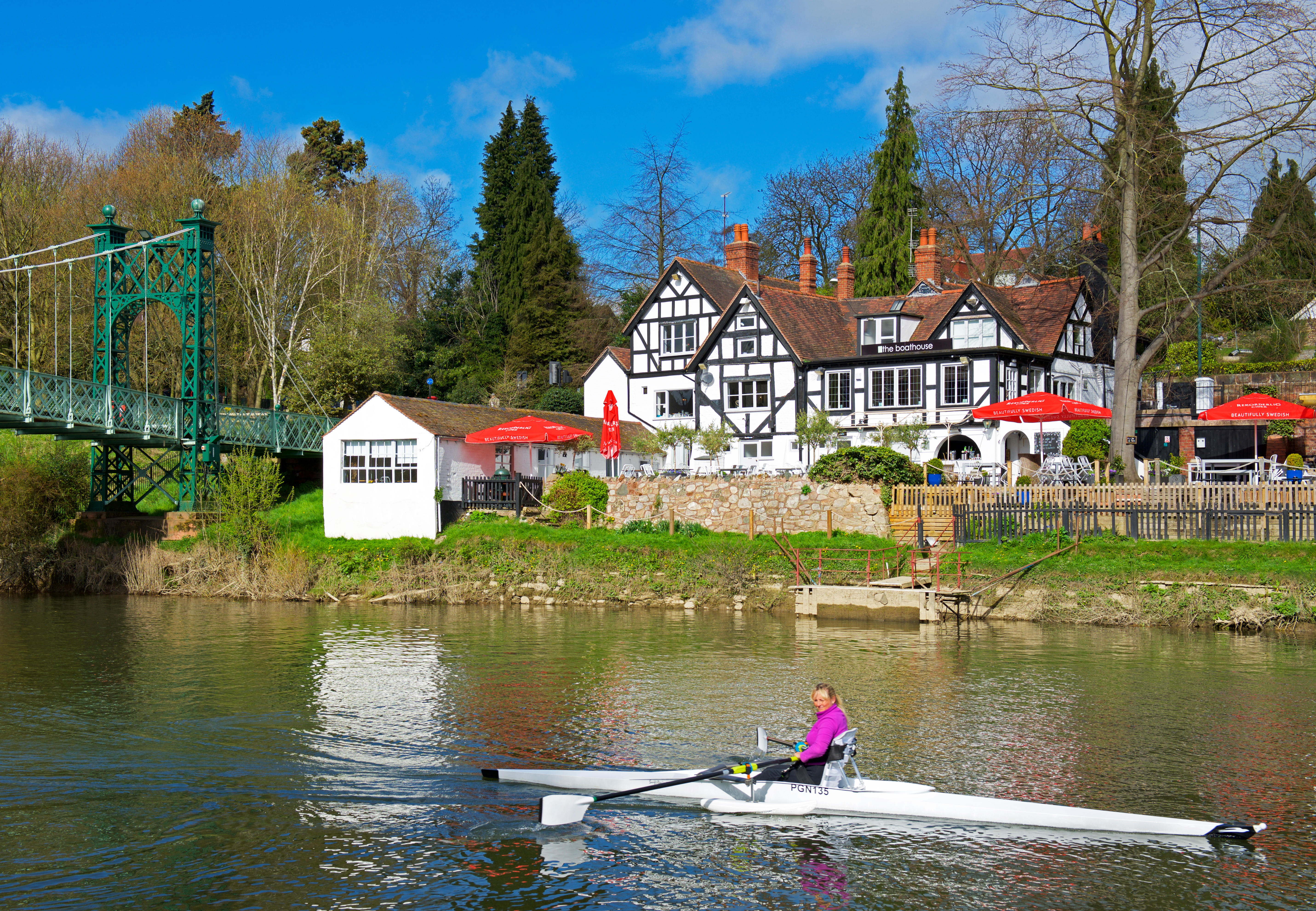 A rower in a boat passes The Boathouse pub on the River Severn in Shrewsbury, England.