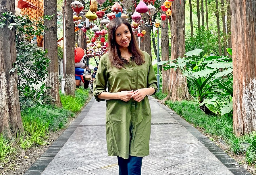 Woman standing on a pathway lined with trees and colorful lanterns.
