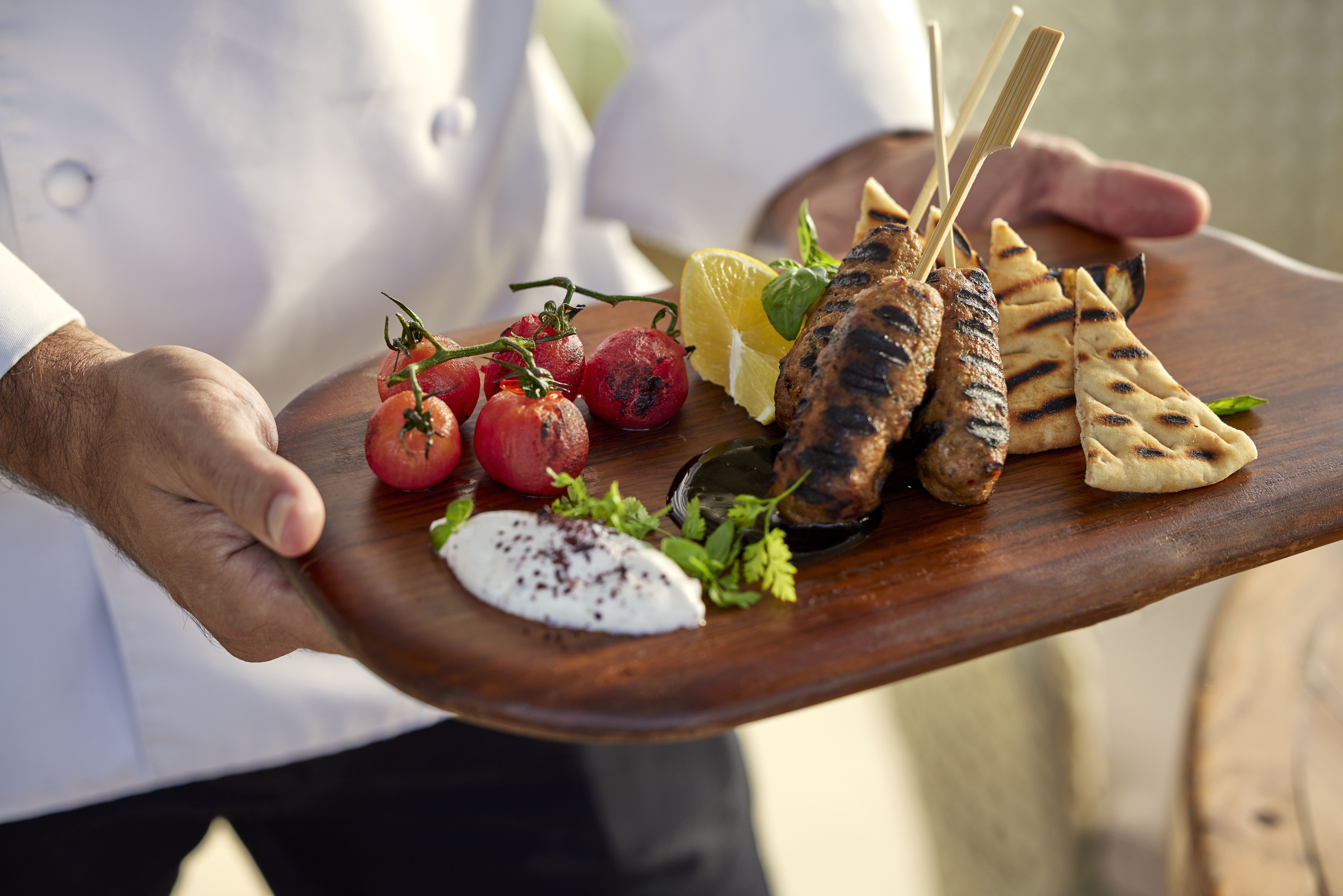 A chef presents grilled meat skewers with roasted tomatoes at Ikos Dassia hotel in Corfu